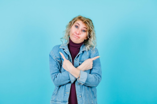 Ontevreden blonde vrouw kijkt naar de camera door vingers te kruisen op een blauwe achtergrond
