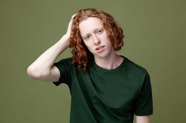 Ontevreden hand op het hoofd zetten jonge knappe kerel met een groen t-shirt geïsoleerd op een groene achtergrond