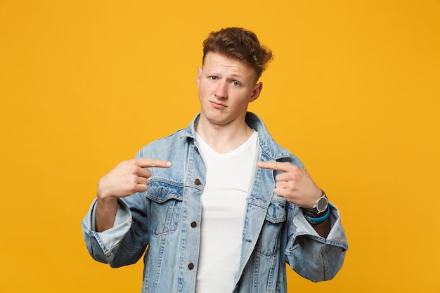 Ontevreden jonge man in denim casual kleding op zoek naar camera, wijzende wijsvingers op zichzelf geïsoleerd op geeloranje muur achtergrond. Mensen oprechte emoties levensstijl concept. Bespotten kopie ruimte.