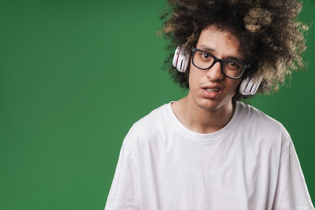 ontevreden man met afro-kapsel die naar voren kijkt terwijl hij een koptelefoon gebruikt die op groen is geïsoleerd