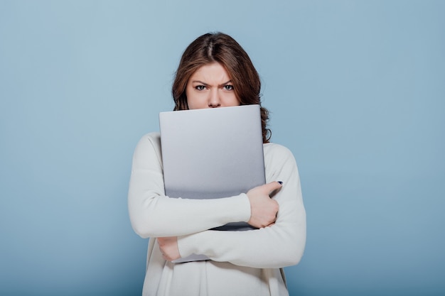 Ontevreden stijlvolle vrouw fronsen terwijl knuffelen laptop geïsoleerd tegen blauwe muur