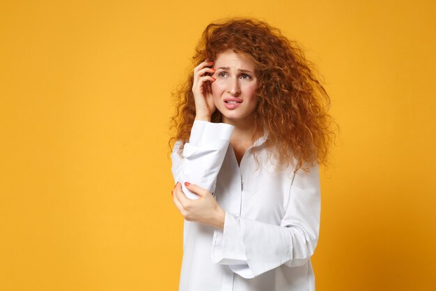 Ontevreden verdrietig jonge roodharige vrouw meisje in wit overhemd poseren geïsoleerd op geel oranje muur