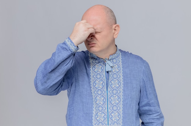 Ontevreden volwassen slavische man in blauw shirt die hand op zijn neus legt