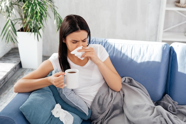 Foto ontevreden vrouw snuit haar neus met gesloten ogen terwijl ze een kop warme drank vasthoudt