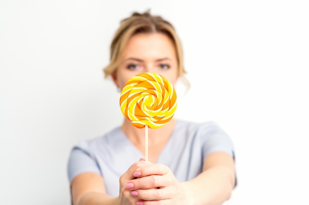 Ontharingsconcept De schoonheidsspecialiste draagt een medische jas met een suikerlolly op een witte achtergrond