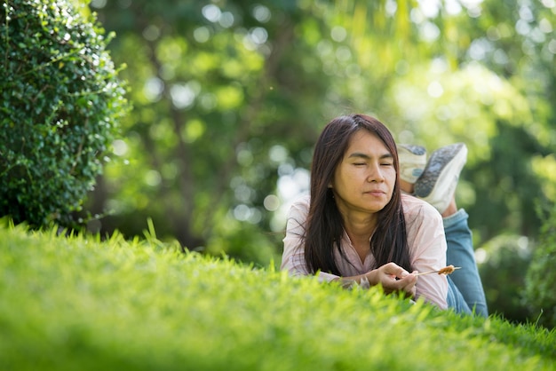 Ontspan mooie aziatische vrouw lachend gezicht liggend op groen grasveld in de buitenlucht tuin park genieten van natuur ochtend Vrijheid Lifestyle vrouw ademen frisse lucht in groen park op lente gazon buitenshuis