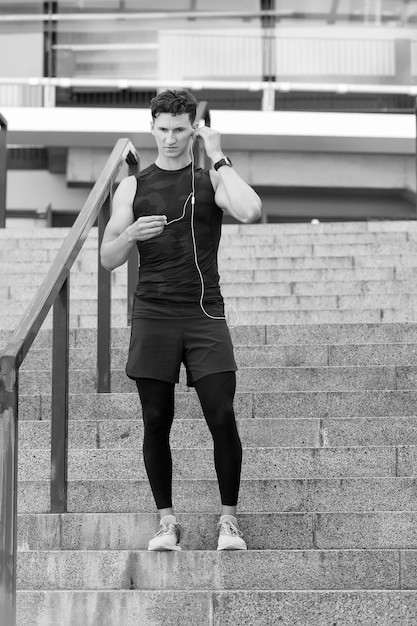 Ontspan na een uitdagende training Runner luistert naar muziek met koptelefoon Fitness sport man met koptelefoon ontspannen postworkout Fit fitness sportmodel muziek buiten voorbereiden voor het joggen