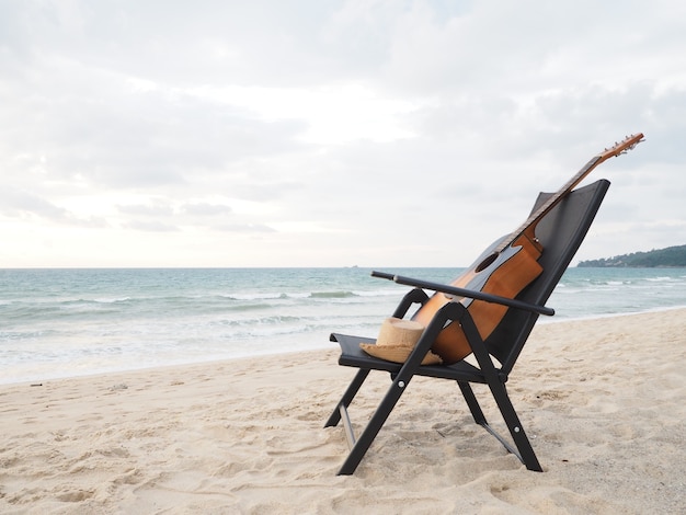 Foto ontspan tijd, akoestische gitaar dichtbij de ligstoel op het strand bij zonsondergang.