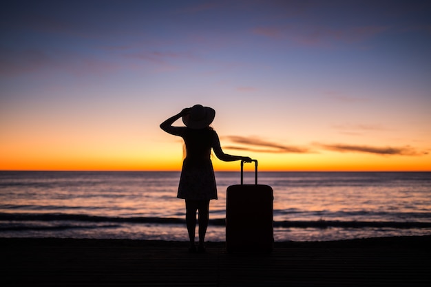 Ontspan vrouw met koffer op een strand bij zonsondergang silhouet vakantie reizen concept jonge dame