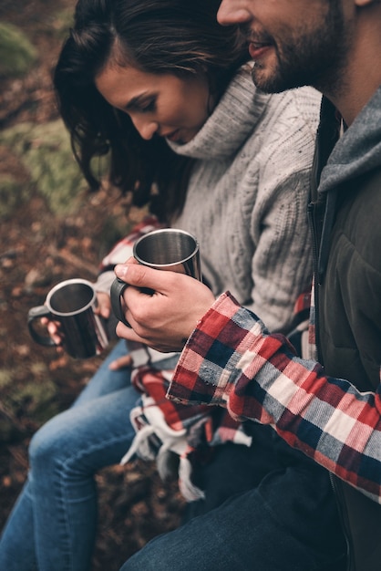 Ontspannen aan de wilde kant. Jong lachend stel geniet van warme dranken terwijl ze in het bos zitten