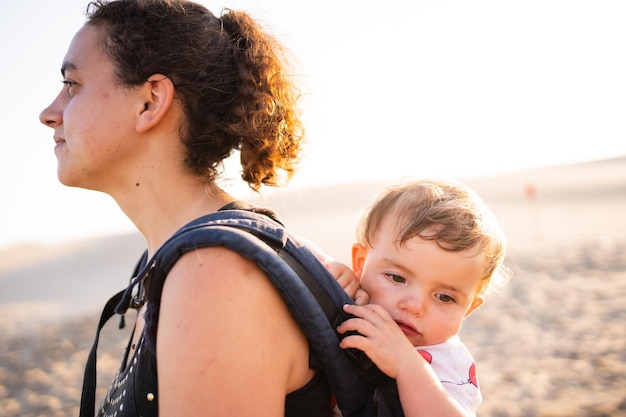 Ontspannen baby op de rug van de moeder in een draagzak buiten tijdens zonsondergang