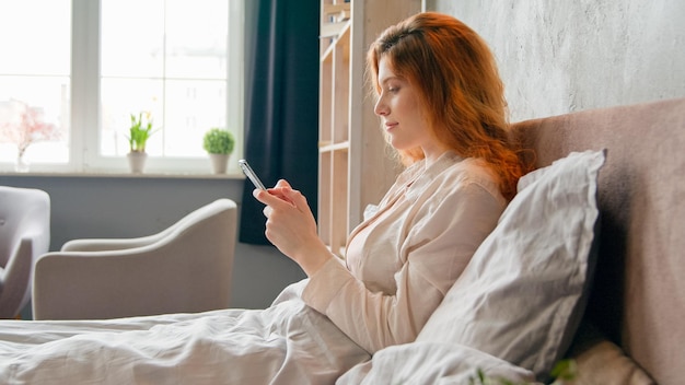 Ontspannen blanke meisjesvrouw in bed bij een rustige ochtendroutine na het wakker worden van een slaapgadget