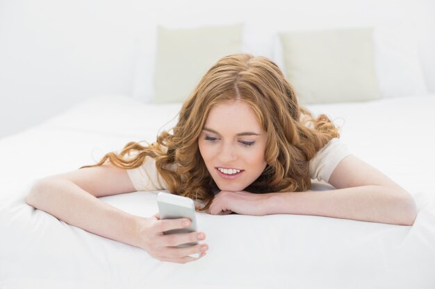 Ontspannen blond die mobiele telefoon in bed bekijken