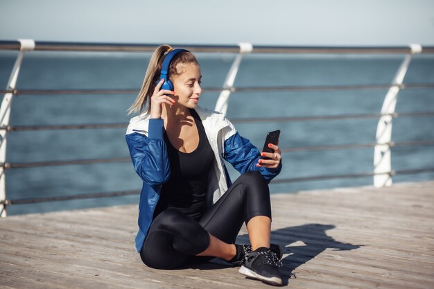 Ontspannen fit vrouw in sportkleding met koptelefoon kiest muziek van een smartphone voor training