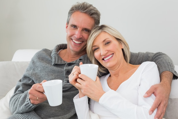 Ontspannen gelukkig paar met koffiekoppen in woonkamer