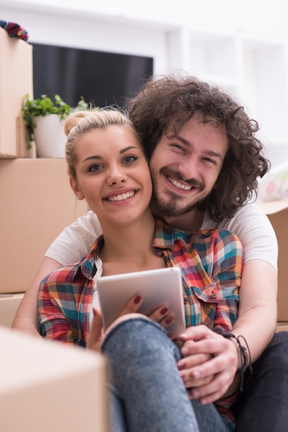 Foto ontspannen in nieuw huis. vrolijk jong stel zittend op de vloer terwijl kartonnen dozen overal om hen heen liggen