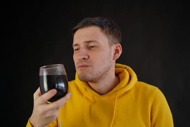 Ontspannen jonge man poseert met glas rode wijn op zwarte achtergrond Volwassen gelukkige man rust met alcohol in zijn weekend
