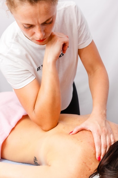 Foto ontspannen jonge vrouw die met het gezicht naar beneden op de massagetafel ligt en geniet van therapeutische lichaamsmassage door professionele masseur in het spa- of wellnesscentrum