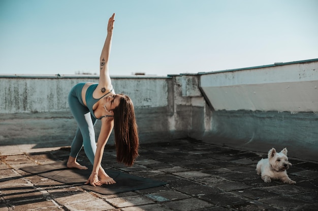 Ontspannen jonge vrouw die yoga beoefent op een dakterras. Ondersteuning door haar hond.