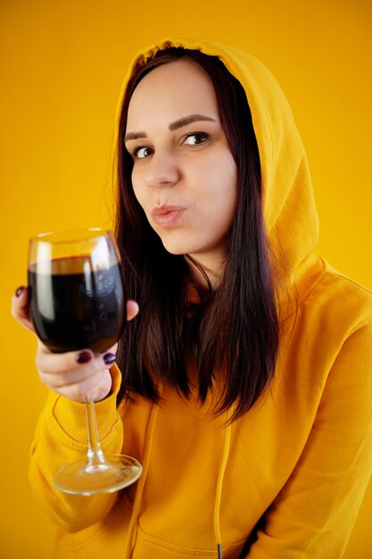 Ontspannen jonge vrouw poseert met een glas rode wijn op een gele achtergrond Volwassen gelukkige brunette rust met alcohol in haar weekend