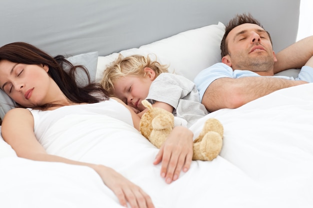 Ontspannen jongetje slaapt met zijn ouders in hun bed