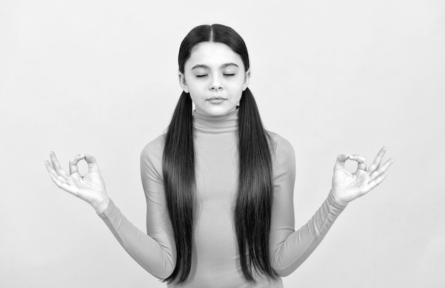 Ontspannen kind met lang haar dat op gele yoga als achtergrond mediteert