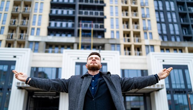 Ontspannen man met geopende armen in de buurt van modern gebouw. Opgewonden zakenman kijkt uit naar nieuwe doelen.