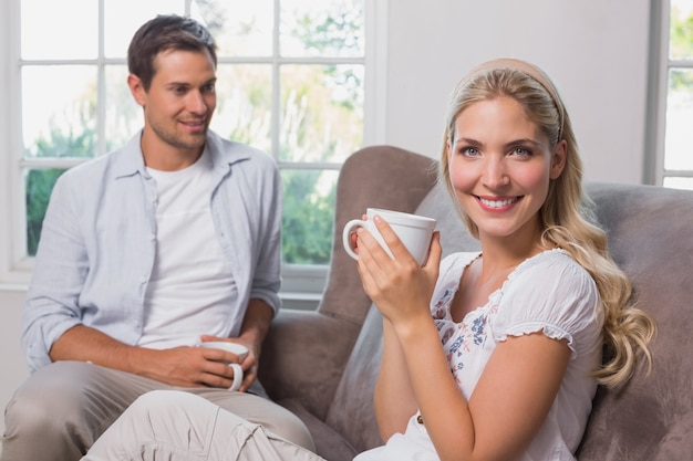 Ontspannen paar met koffiekoppen die in woonkamer zitten