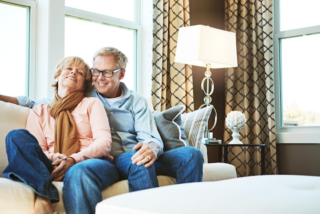 Foto ontspannen thuis en volwassen paar op de bank knuffelen voor het binden van gezonde relatie en huwelijk pensioen gelukkig en senior man en vrouw glimlachen op de bank voor liefde toewijding en omhelzen in de woonkamer