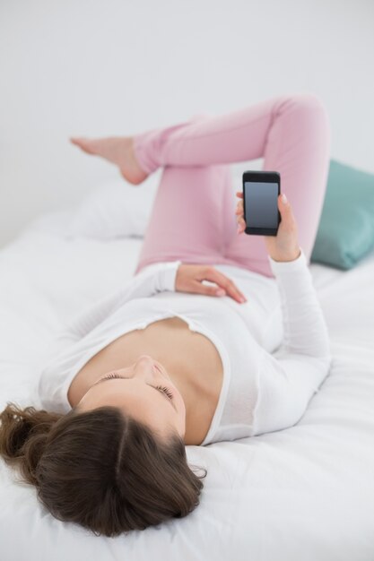 Ontspannen vrouw die mobiele telefoon in bed bekijkt