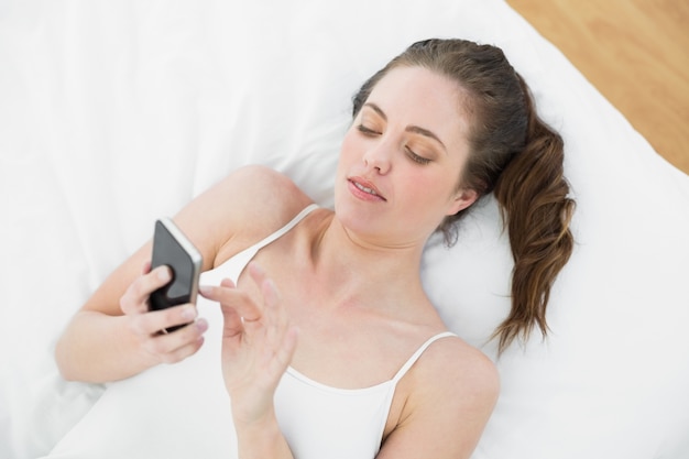 Ontspannen vrouw die mobiele telefoon in bed met behulp van