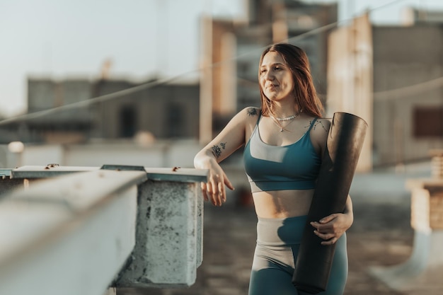 Ontspannen vrouw houdt oefenmat vast en bereidt zich voor op het beoefenen van yoga op een dakterras.