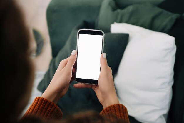 Foto ontspannen vrouw met behulp van smartphone-apps op de bank thuis over de schouder weergave met mobiele telefoon display mock