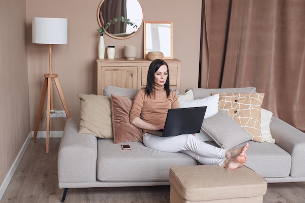 Ontspannen vrouw op de bank met laptop die thuis werkt