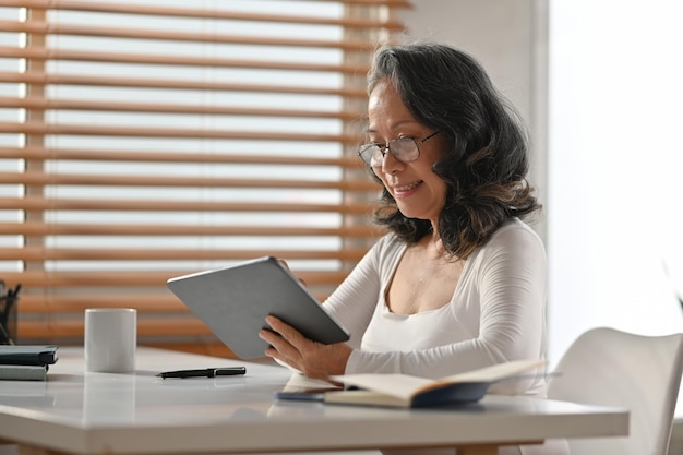 Ontspannen vrouw van middelbare leeftijd die online nieuws leest of e-commerce aanbiedingen zoekt op digitale tablet thuis