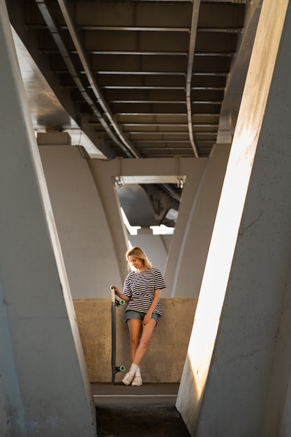 Ontspannen vrouw van middelbare leeftijd geniet van de zonsondergang van afgelopen zomer onder een stadsbrug met longboard