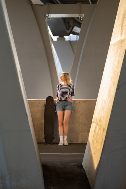 Ontspannen vrouw van middelbare leeftijd geniet van de zonsondergang van afgelopen zomer onder een stadsbrug met longboard