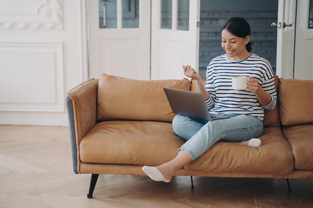 Ontspannen vrouw werkt vanuit huis en drinkt koffie Lady zit op de bank en vergadert online