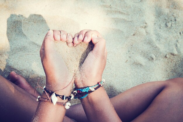 Ontspanning en vrije tijd in de zomer levensstijl afbeelding van een slank gelooid meisje op het strand, met een zand hart symbool in de hand. Op handen zijn veel zeeschelp armbanden. Tropisch eiland strand