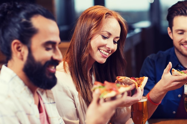 ontspanning, eten en drinken, mensen en vakanties concept - glimlachende vrienden die pizza eten en bier drinken in een restaurant of pub