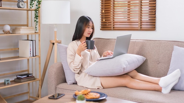 Ontspanning lifestyle concept Jonge Aziatische vrouw surfen op sociale media op laptop en koffie drinken