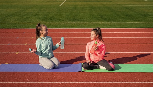 Ontspanningsoefeningen kinderen in sportkleding ontspannen op yogamat kinderen oefenen op het goede spoor gezonde jeugdtraining op frisse lucht buiten dorst en hydratatie tienermeisjes drinken water op stadion