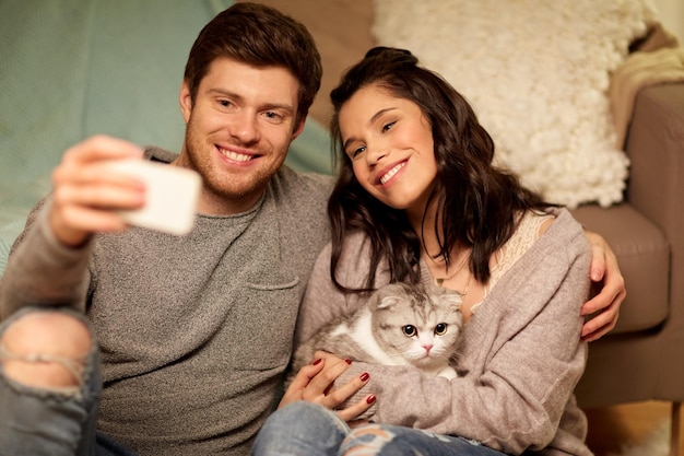Foto ontspanningstechnologie en mensenconcept gelukkig stel met kat die thuis selfie maakt met hun smartphone