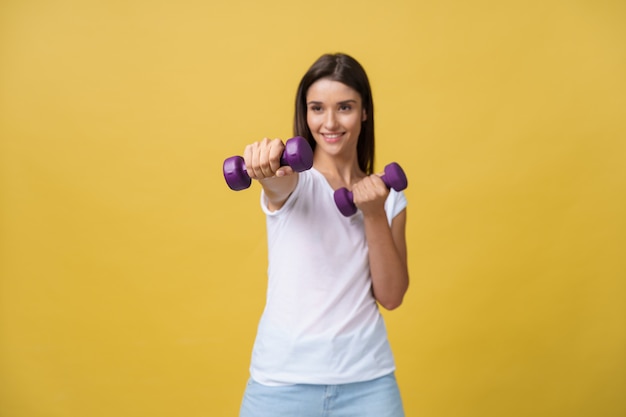 Ontsproten van een mooie en sportieve jonge vrouw die gewichten opheffen tegen gele achtergrond.