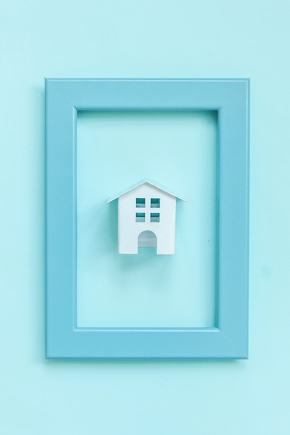 Ontwerp eenvoudig met miniatuur wit stuk speelgoed huis in blauw frame dat op blauwe kleurrijke pastelkleur wordt geïsoleerd