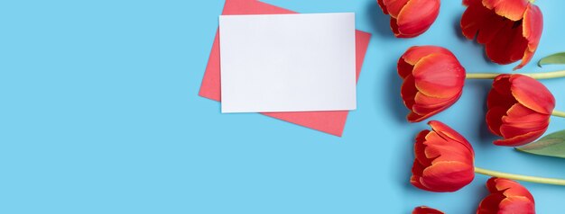 Ontwerpconcept van Moederdag vakantie groet cadeau ontwerp met rode tulp boeket en kaart op heldere blauwe tafel achtergrond
