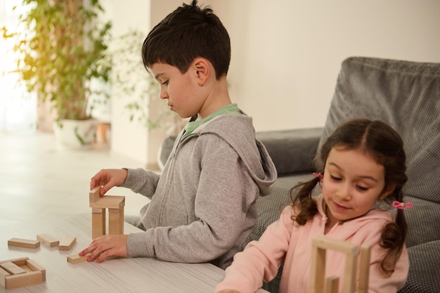 Ontwikkeling van fijne motoriek en concentratie, educatieve vrije tijd, familietijdverdrijfconcept. Gerichte kinderen die constructies bouwen met houten blokken, bordspellen spelen in de huiskamer.