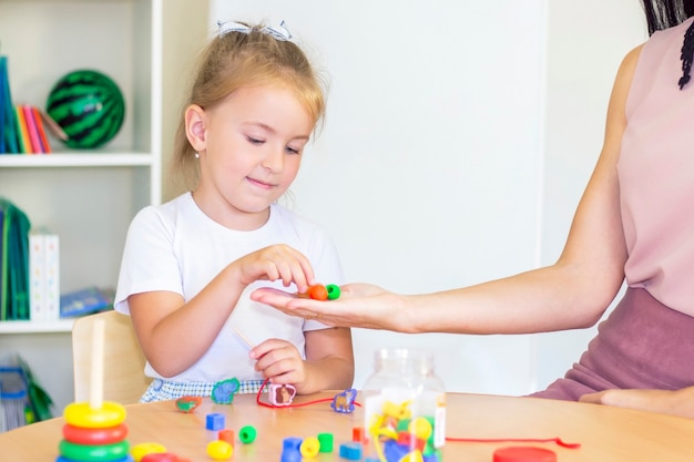 Ontwikkelings- en logopedische lessen met een kindmeisje. Logopedie-oefeningen en spelletjes met kralen. Het meisje heeft kralen in haar handen