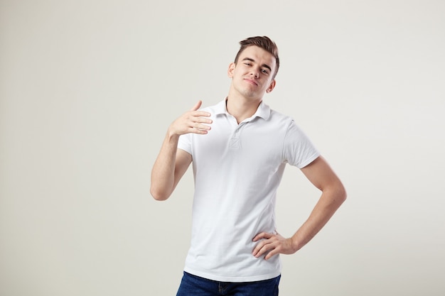 Onverschillige man gekleed in een wit t-shirt en jeans is op een witte achtergrond in de studio.