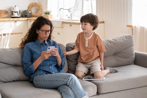 Onverschillige moeder surft op sociale media geïrriteerd door afleidende verveelde kleine zoon heeft mama-aandacht nodig